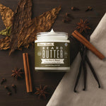 Open jar of Tallow Man Tobacco Vanilla Beard + Body Butter with tobacco leaf, vanilla beans, cinnamon, star anise and cloves on dark wood.